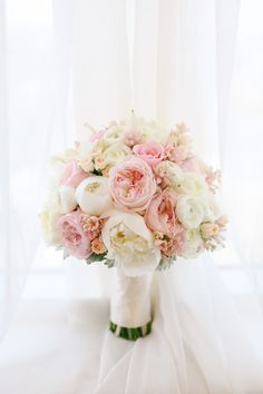 a bridal bouquet with pink and white flowers in front of a curtained window