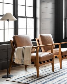 two leather chairs sitting next to each other on top of a rug in front of windows