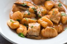 a white bowl filled with meat covered in gravy and garnished with parsley