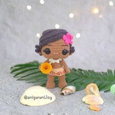 a small crocheted doll standing next to some seashells and palm leaves