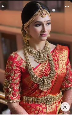 a woman in a red and gold sari with jewelry on her neck, smiling at the camera