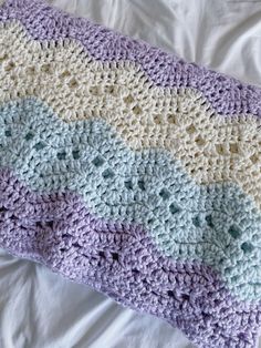 a crocheted blanket laying on top of a bed next to a white pillow