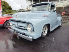 an old blue truck parked in front of a red and white car on a wet parking lot