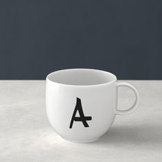 a white coffee cup with the letter a on it's side, sitting on a table