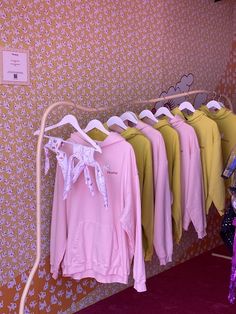 several pink and yellow shirts are hanging on a rack in front of a wallpapered background