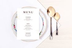 a table setting with a menu and silverware on it, along with two gold - plated utensils