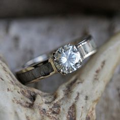 a diamond ring sitting on top of a piece of driftwood in front of a stone wall