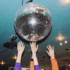 two people reaching for a disco ball in the air with their hands up to it