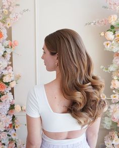 a woman with long hair standing in front of a flower wall wearing a white top