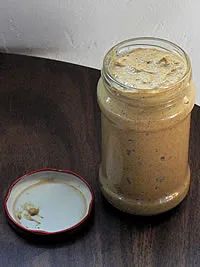 a glass jar filled with peanut butter sitting on top of a wooden table next to a plate