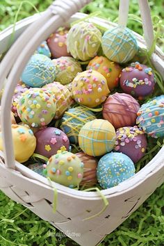 a basket full of decorated easter eggs on the grass with sprinkles in it