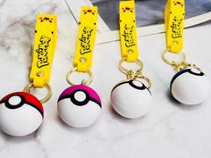 four pokemon ball keychains are shown on a marble counter with a yellow lanyard