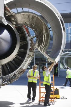 two men in safety vests standing next to an airplane engine