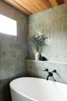 a white bath tub sitting next to a window in a room with wooden ceilinging