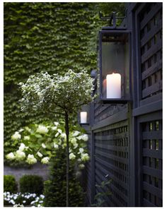 a candle is lit in front of a wall with white flowers and greenery behind it