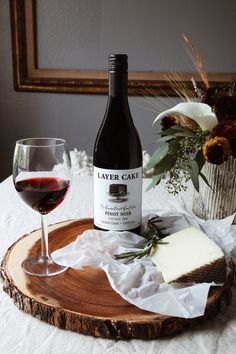 a bottle of wine and some cheese on a wooden tray next to a glass of red wine