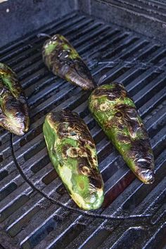 four green peppers are on the grill and one has been grilled to eat them