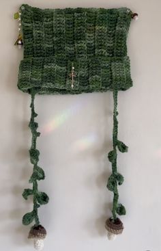 a green knitted hat hanging on the wall with tassels and bells attached to it