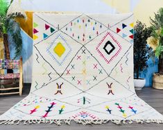 a white rug with multicolored designs on the floor next to potted plants