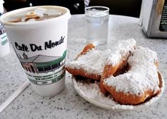 powdered sugar covered doughnuts on a plate next to a cup of coffee