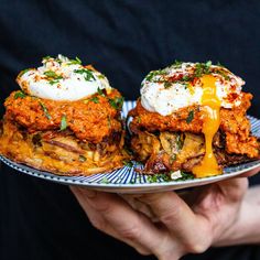 a person holding a plate with two food items on it and sauce drizzled over them