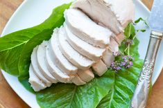 a white plate topped with sliced turkey and lettuce next to a knife on top of a wooden table