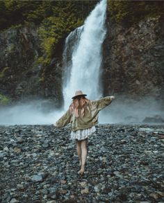 a woman standing in front of a waterfall with her arms spread out to the side