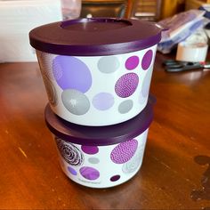 two purple and white cups sitting on top of a wooden table next to each other