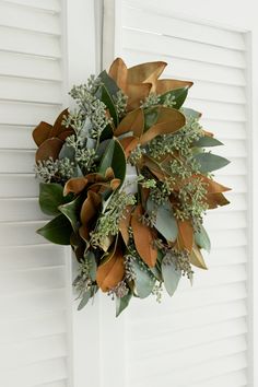 a wreath hanging on the side of a door with leaves and greenery around it