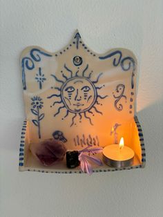 a candle is lit in front of a ceramic plate with an image of the sun on it