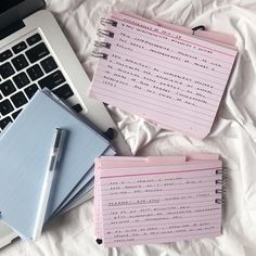 three notebooks sitting on top of a bed next to a laptop computer and keyboard