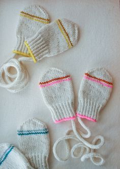 three knitted mittens and two pairs of gloves on a white surface with yarn