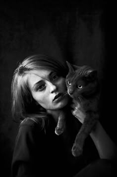 a black and white photo of a woman holding a cat in her arms, looking at the camera