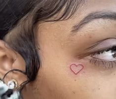 a woman's eye with a red heart tattoo on her left cheek and behind her ear