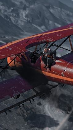 a man is sitting on the wing of an old biplane flying over a mountain range