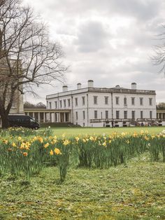 a large white house sitting on top of a lush green field next to trees and flowers