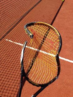 a tennis racket and ball laying on the ground next to a net with white lines