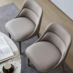 two chairs sitting on top of a rug next to a table with an open book