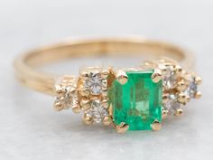 an emerald and diamond ring on a white surface