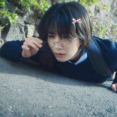 a person laying on the ground wearing glasses and a blue shirt with pink bows in their hair