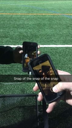 two people holding up their cell phones to take pictures on the same screen as they stand in front of a soccer field