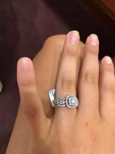 a woman's hand with a diamond ring on top of her finger and the other hand holding an engagement ring