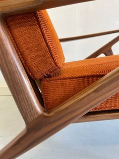 a wooden chair with an orange cushion on the back and armrests is shown