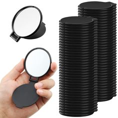 a hand holding a magnifying glass next to a stack of black round mirrors