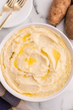 a white bowl filled with mashed potatoes on top of a marble counter next to goldware