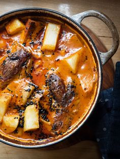 a pot filled with stew and potatoes on top of a wooden table