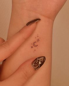 a woman's hand with a small tattoo on her left wrist and the moon behind it