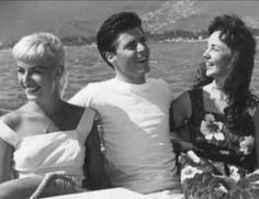 three women and a man sitting on a boat in the water, smiling at each other