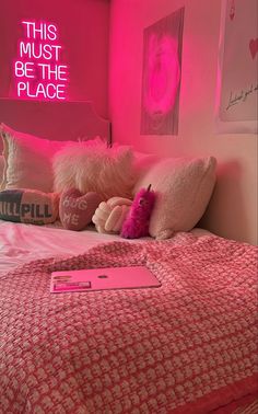 a bed with pink sheets and pillows in a room that has a neon sign on the wall