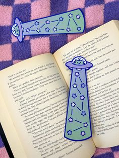 an open book with a tie and stars on it next to another bookmark that is shaped like a spaceship